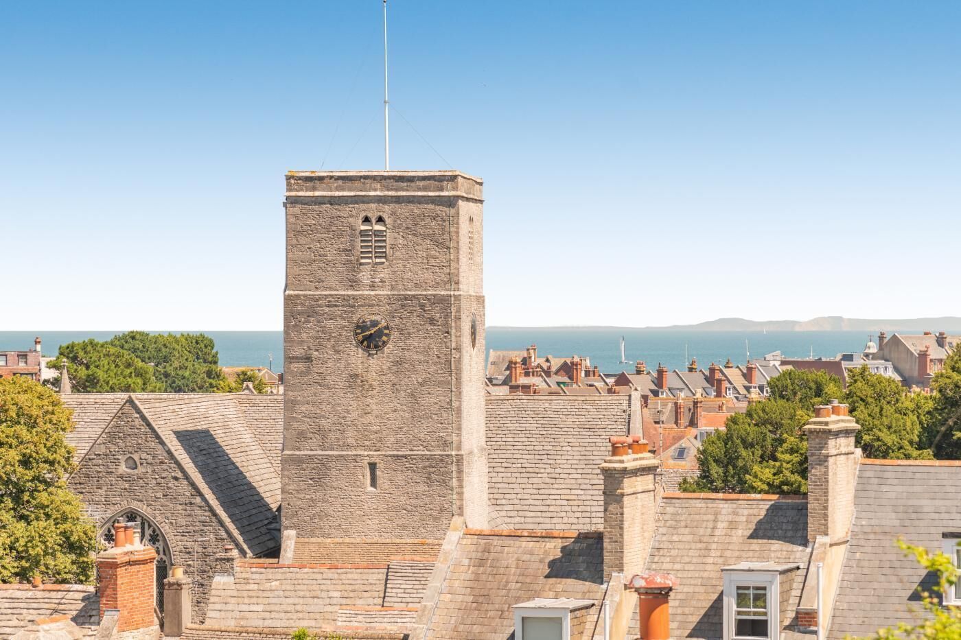 Ein historischer Steinturm mit Uhr, umgeben von traditionellen terrassenförmig angelegten Häusern mit Blick auf das Meer.