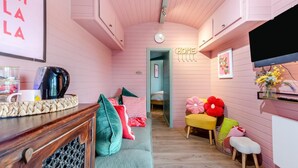 Een knus interieur met een houten plafond, een bank met kleurrijke kussens, een tafeltje met een waterkoker en een aan de muur bevestigde televisie.