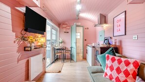 Een gezellige keuken met een eethoek, een televisie aan de muur en een bank met een rood-wit geblokt kussen.