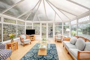 A conservatory with a stone wall, a television, and seating areas. - 3 Bed in Dolgellau (oc-203224) (Llanelltyd)