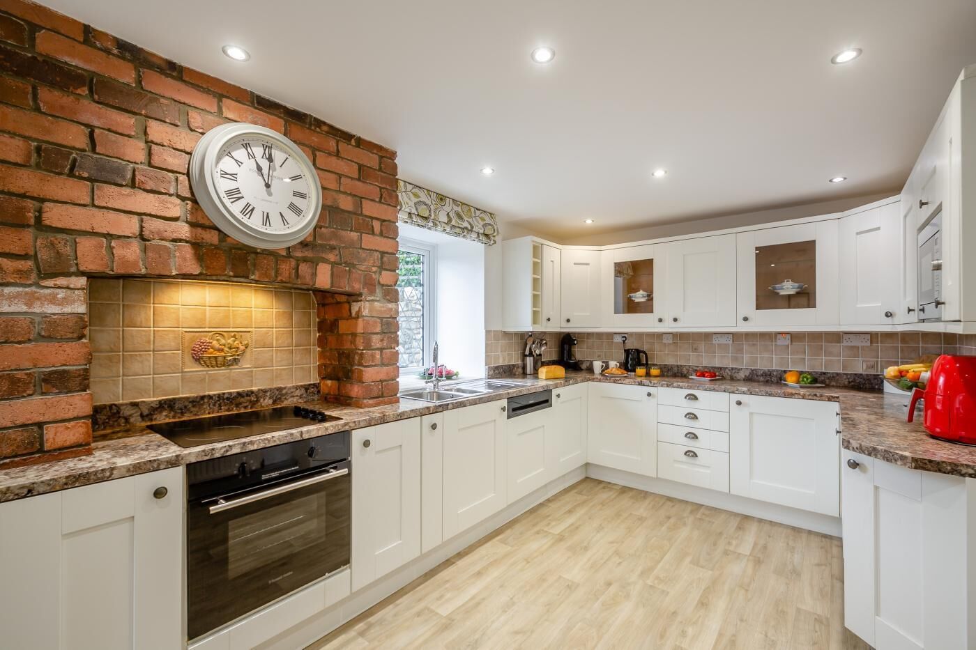 A kitchen with white cabinets, a brick wall, a built-in oven, and a clock.