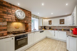 A kitchen with white cabinets, a brick wall, a built-in oven, and a clock. - 3 Bed in Dolgellau (oc-203224) (Llanelltyd)