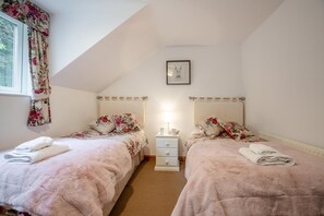 A bedroom with two beds, a nightstand, a framed picture, and a window with floral curtains. - 3 Bed in Dolgellau (oc-203224) (Llanelltyd)