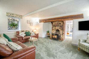 A cozy living room with a stone fireplace, leather sofas, and a television mounted on the wall. - 3 Bed in Dolgellau (oc-203224) (Llanelltyd)