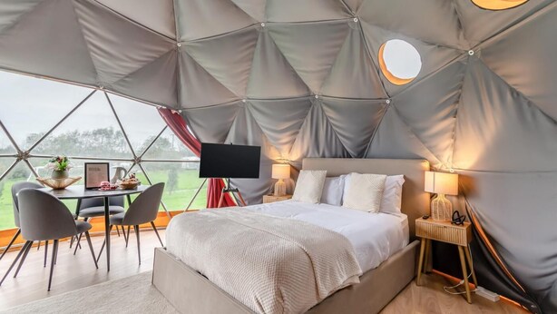 Een ruime tentkamer met een bed, nachtkastje, lamp en een flatscreen televisie.