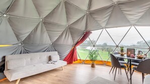 Een geometrisch koepelkamertje met een bank, eettafel, stoelen en uitzicht op de omgeving.
