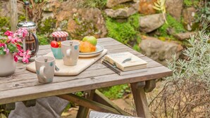Una mesa de picnic de madera con un libro, una tetera, una taza, un tarro y un plato con comida.