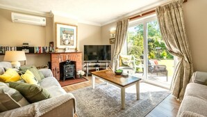 A cozy living room with a fireplace, a television, and a large window with curtains. - 2 Bed in Hickling (oc-1794) (Hickling)