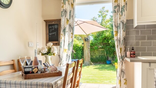 A cozy dining area with a table set for two, a chalkboard with a holiday message, and a view of a lush garden through open curtains. - 2 Bed in Hickling (oc-1794) (Hickling)