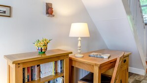 A corner room with a wooden desk, a bookshelf, a lamp, and a vase with flowers. - 2 Bed in Pooley Bridge (oc-r33740) (Pooley Bridge)