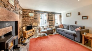 A cozy living room with a stone wall, a fireplace, a sofa, and a television. - 2 Bed in Pooley Bridge (oc-r33740) (Pooley Bridge)