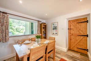A dining room with a wooden table set for four, a bookshelf, and a large wooden door. - 2 Bed in Pooley Bridge (oc-r33740) (Pooley Bridge)