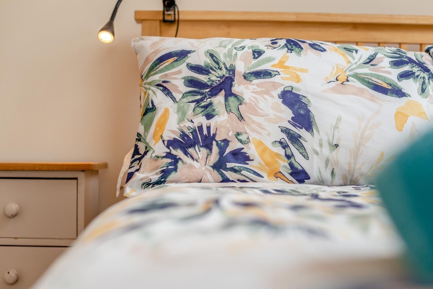 Una cama con una colcha de estampado floral, un cabecero de madera y una mesita de noche con una lámpara.