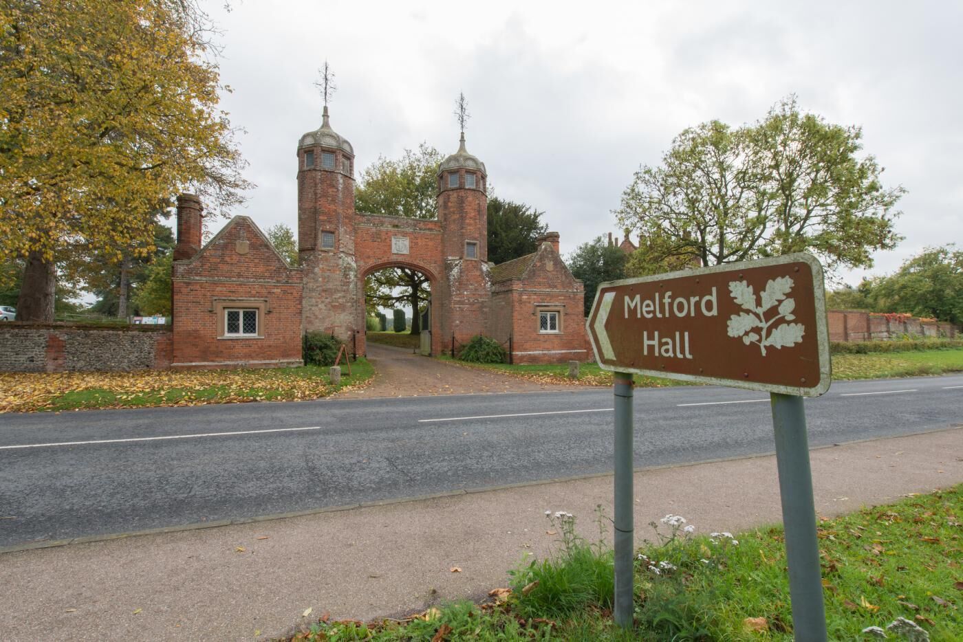 Une enseigne indiquant l’entrée de Melford Hall, avec une arche en briques et des tours en arrière-plan.
