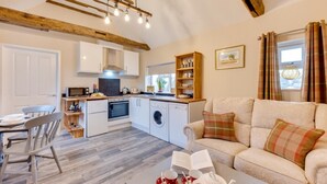 Een moderne keuken met witte kastjes, een inbouwoven en een wasmachine. Er is een eethoek met een tafel en stoelen, en een woonkamer met een bank en salontafel.