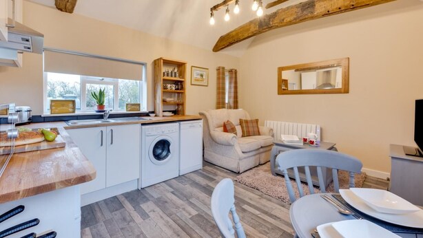 Een kleine keuken met een wasmachine, een eethoek met een tafel en stoelen, en een zithoek met een bank.