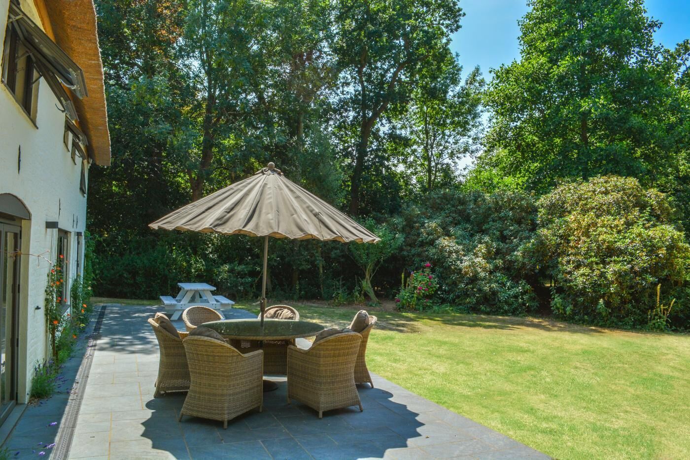 An outdoor patio with wicker furniture, a table, and a large umbrella.