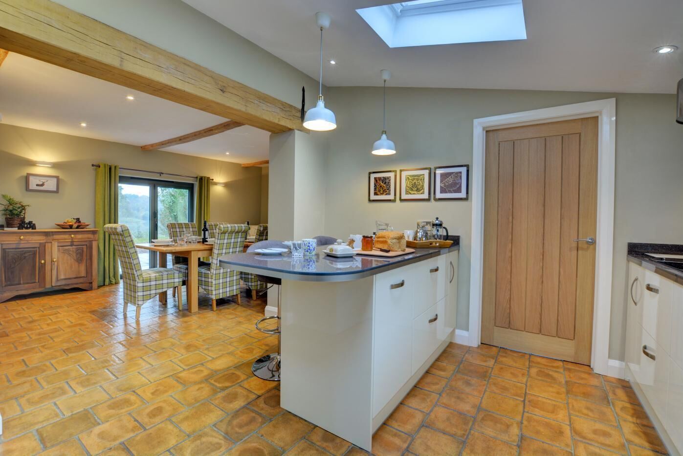 Una cocina con isla central, vigas de madera, zona de comedor con sillas y vistas por una ventana.
