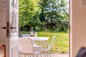 An outdoor dining area with a table and chairs, a bottle of wine, and a glass. - 3 Bed in Dunwich (oc-atc2) (Dunwich)