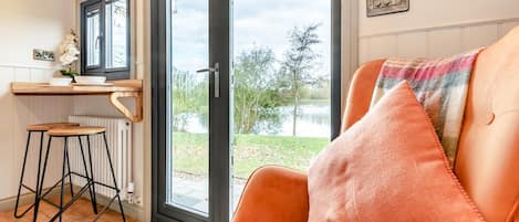 Una habitación acogedora con sofá, una mesita con un cuenco y una planta, y vistas a un lago a través de un ventanal.