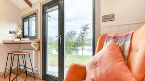 Tunnelmallinen huone, jossa on sohva, pieni pöytä, jossa on kulho ja kasvi, ja lasiovesta avautuu näkymä järvelle.