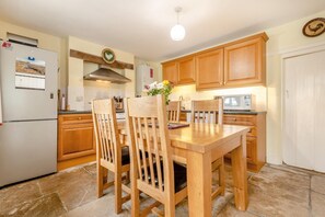 A kitchen with wooden cabinets, a dining table with chairs, a refrigerator, and a stove. - 3 Bed in Weymouth (oc-s33545) (Weymouth)