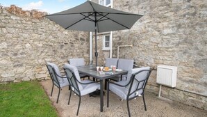 Ein Steinhaus mit Terrassentisch und -stühlen, einem großen Sonnenschirm und einer Steckdose an der Wand.