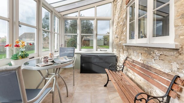 Ein Wintergarten mit Tisch und Stühlen, einer Bank und Blick auf den Garten.
