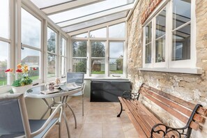 A conservatory with a table and chairs, a bench, and a view of the garden. - 3 Bed in Weymouth (oc-s33545) (Weymouth)