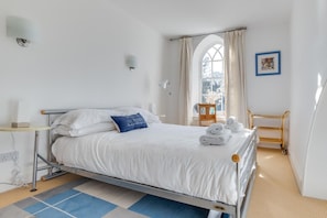 A neatly made bed with white linens and a blue pillow, a small bedside table with a lamp, a window with curtains, and a framed picture on the wall. - 2 Bed in Embleton (oc-nb1960) (Embleton)