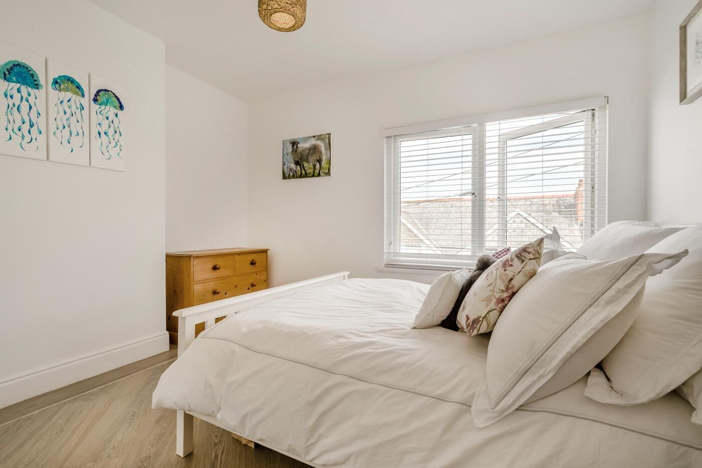 Un dormitorio con cama, cómoda de madera, ventana con persianas y decoración en la pared.