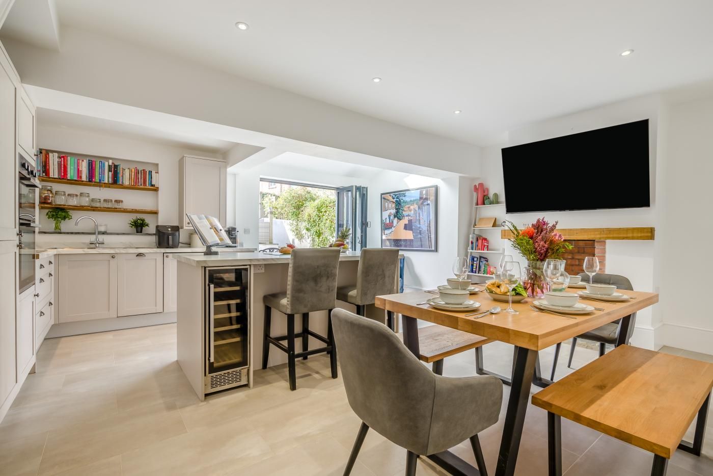 Una cucina moderna con un'elegante cantinella integrata, un'area pranzo con tavolo e sedie in legno e un grande televisore a schermo piatto fissato al muro.