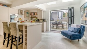 A modern kitchen with a central island, a dining area with a table and chairs, and a blue sofa in a bright living space. - 3 Bed in Padstow (oc-f33036) (Padstow)