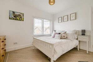 A bedroom with a white bed, a nightstand, a dresser, and a window with blinds. - 3 Bed in Padstow (oc-f33036) (Padstow)