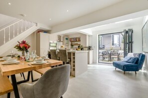 A modern kitchen with white cabinets, a dining area with a wooden table set for four, and a blue armchair in a bright living space with a staircase. - 3 Bed in Padstow (oc-f33036) (Padstow)