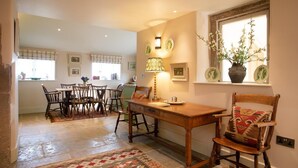 A dining area with a wooden table and chairs, a patterned rug, and wall-mounted light fixtures.