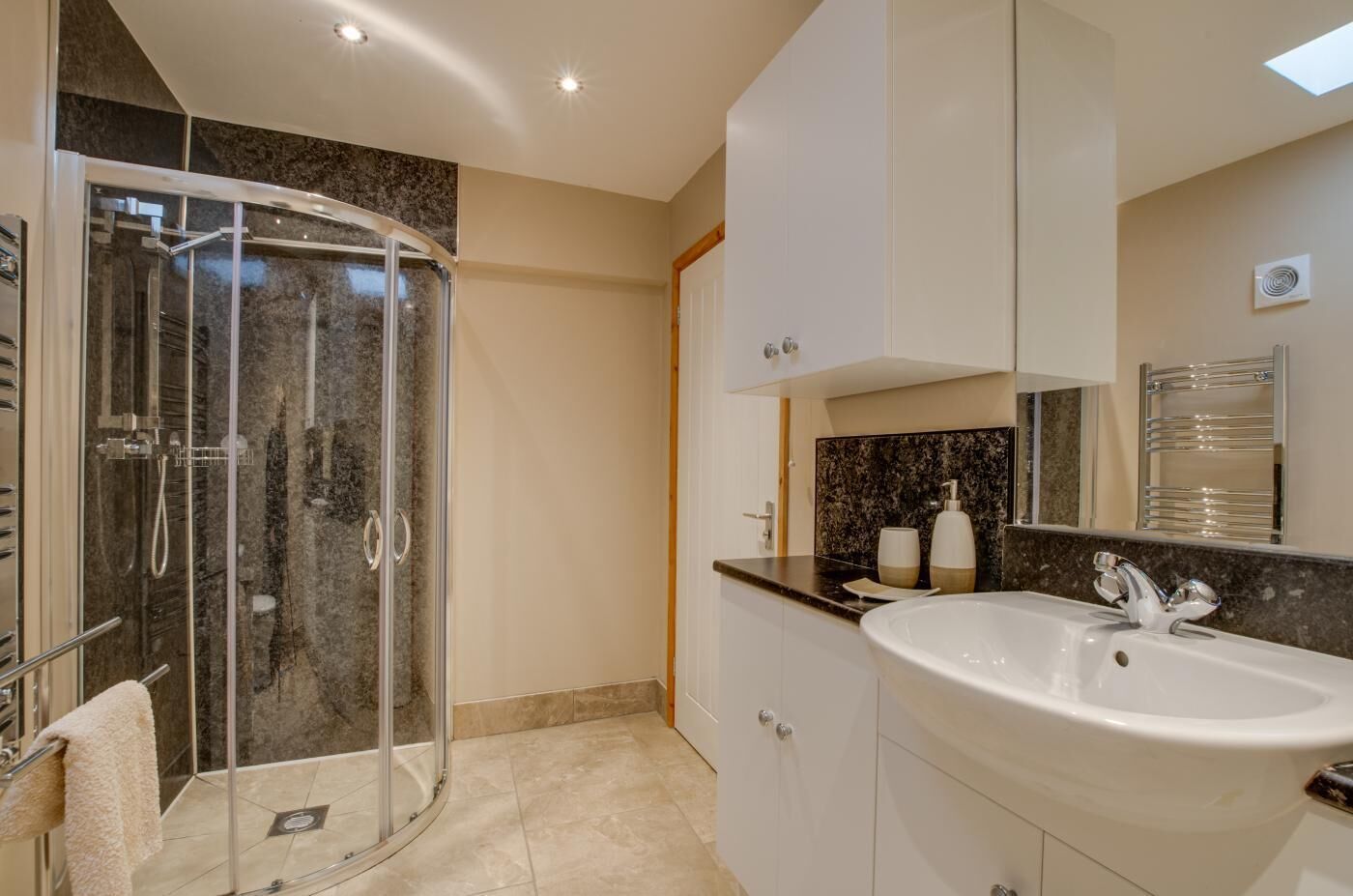 A modern bathroom with a glass-enclosed shower, a white sink, and a marble-tiled floor.