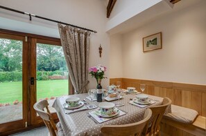 A dining area with a table set for four, a vase with flowers, and a view of a garden through a glass door. - 2 Bed in Machynlleth (oc-491245) (Llanwrin)