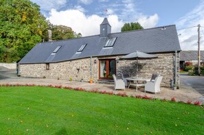A stone building with a sloped roof, a chimney, and a small porch with outdoor seating. - 2 Bed in Machynlleth (oc-491245) (Llanwrin)