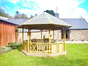 A wooden gazebo with a roof, surrounded by a well-maintained lawn and a stone building in the background. - 2 Bed in Machynlleth (oc-491245) (Llanwrin)