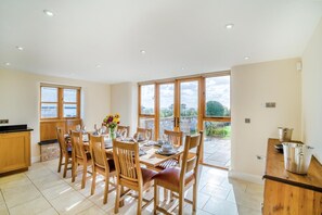 A dining area with a large table set for six, wooden chairs, and a view of a garden through large windows.