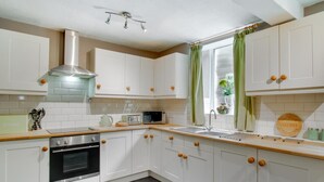 Una cocina moderna con armarios blancos, una campana extractora de acero inoxidable, horno empotrado, un fregadero y un ventanal con cortinas verdes.