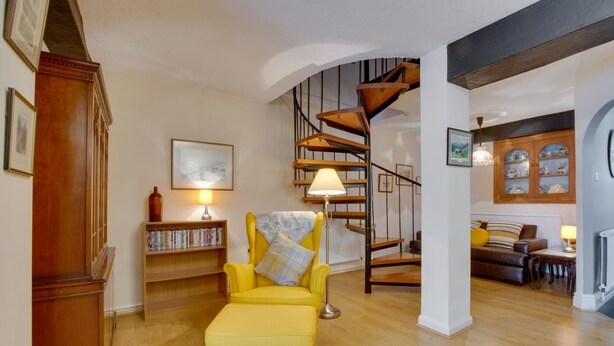 Una sala de estar con un sillón amarillo, una escalera de madera, estanterías y una chimenea.