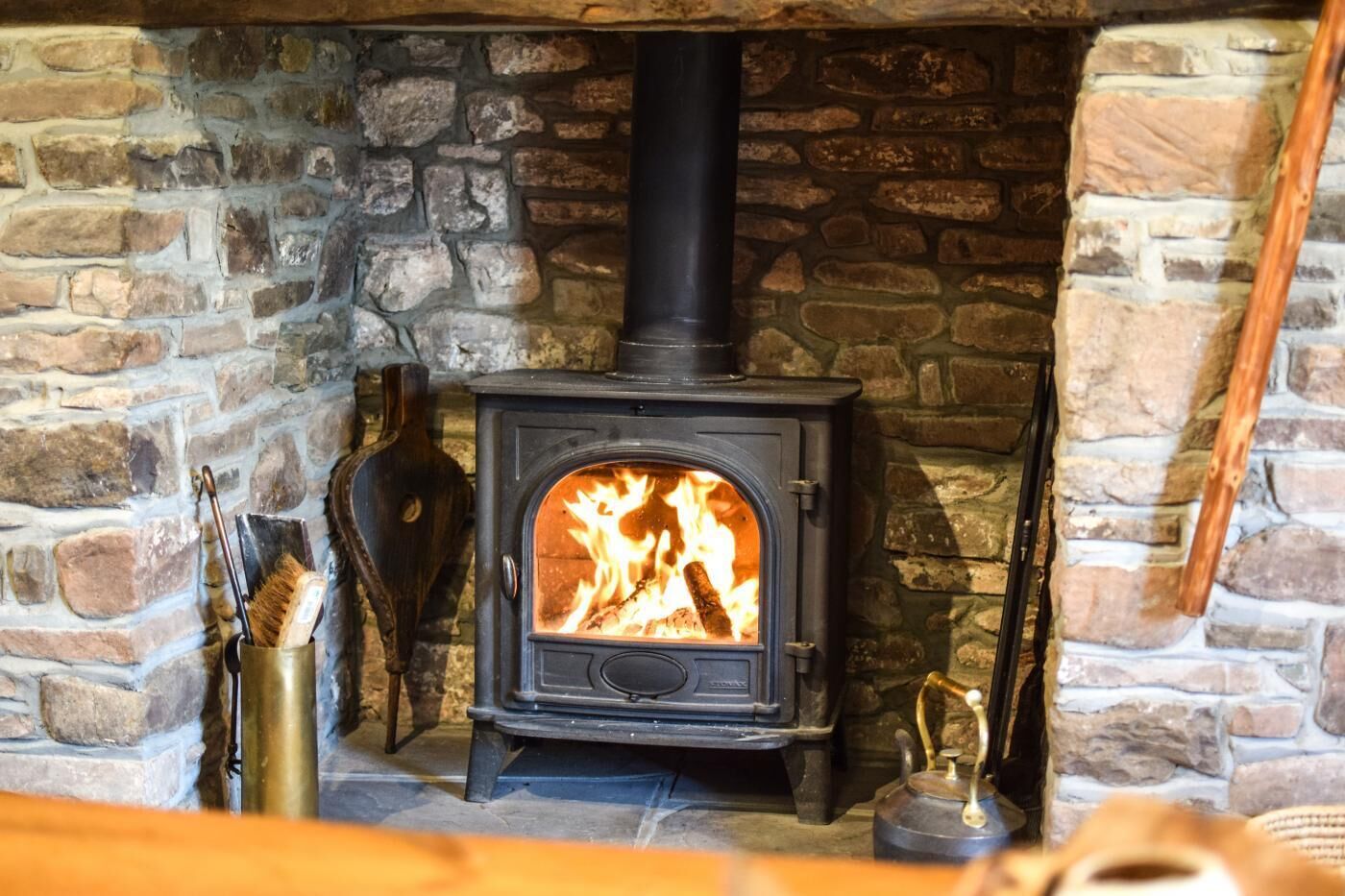 Une cheminée en pierre avec un poêle à bois noir, une bouilloire en métal et une cuillère en bois.