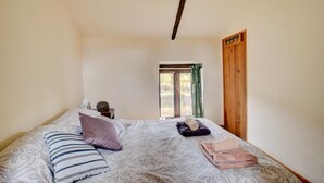 Un dormitorio con cama, almohadas, mesita de noche, ventana y puerta de madera.