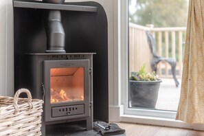 A wood-burning stove with a glass front, positioned next to a window with a view of a balcony.