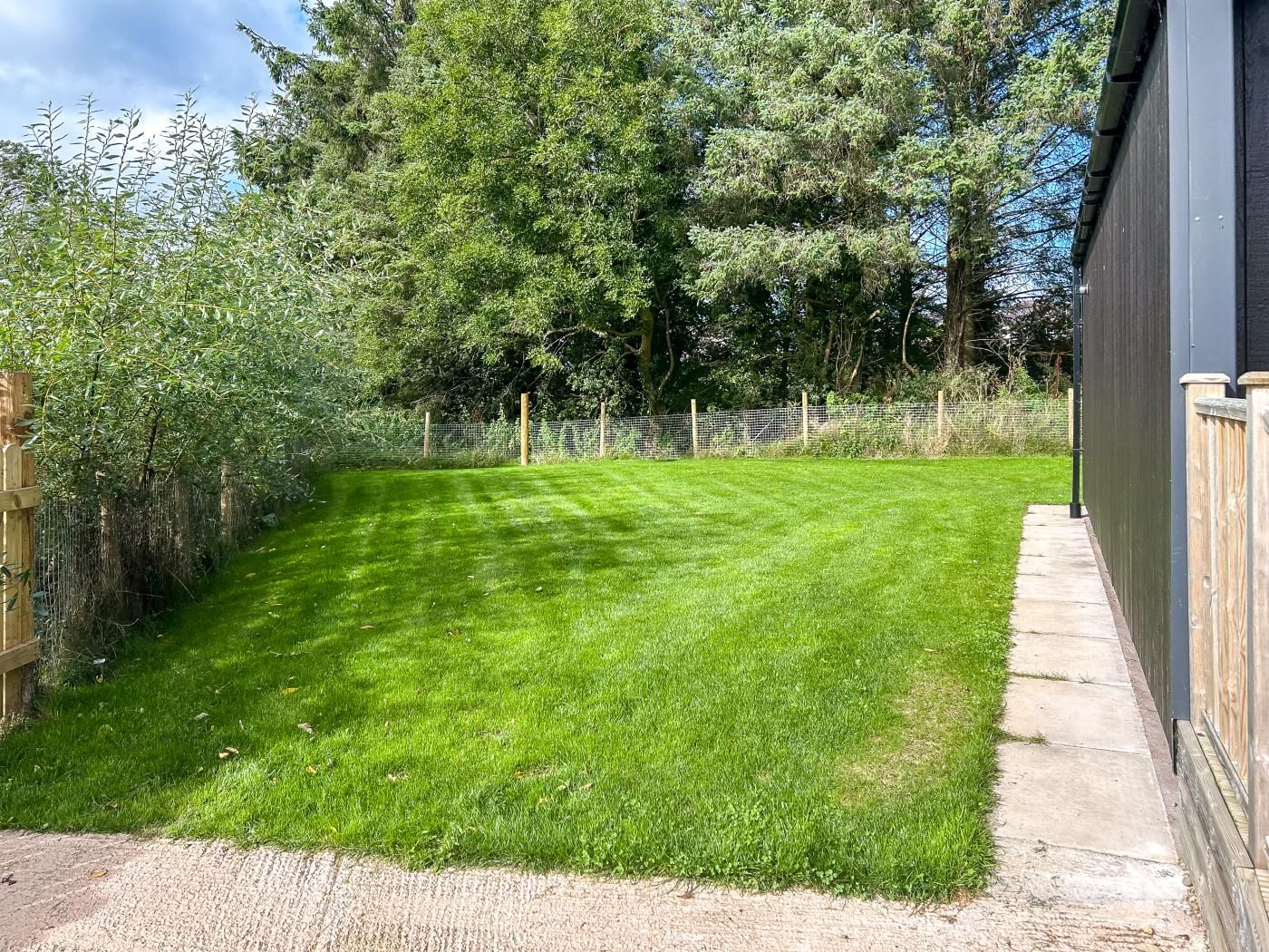 A well-maintained grassy yard with a wooden fence, a concrete path, and a wooden deck adjacent to a building.