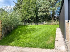A well-maintained grassy yard with a wooden fence, a concrete path, and a wooden deck adjacent to a building.