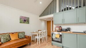 A cozy living room with a brown leather sofa, a dining table with chairs, and a kitchen area with light green cabinets and a wooden countertop. - 2 Bed in Mouswald (oc-b33444) (Mouswald)