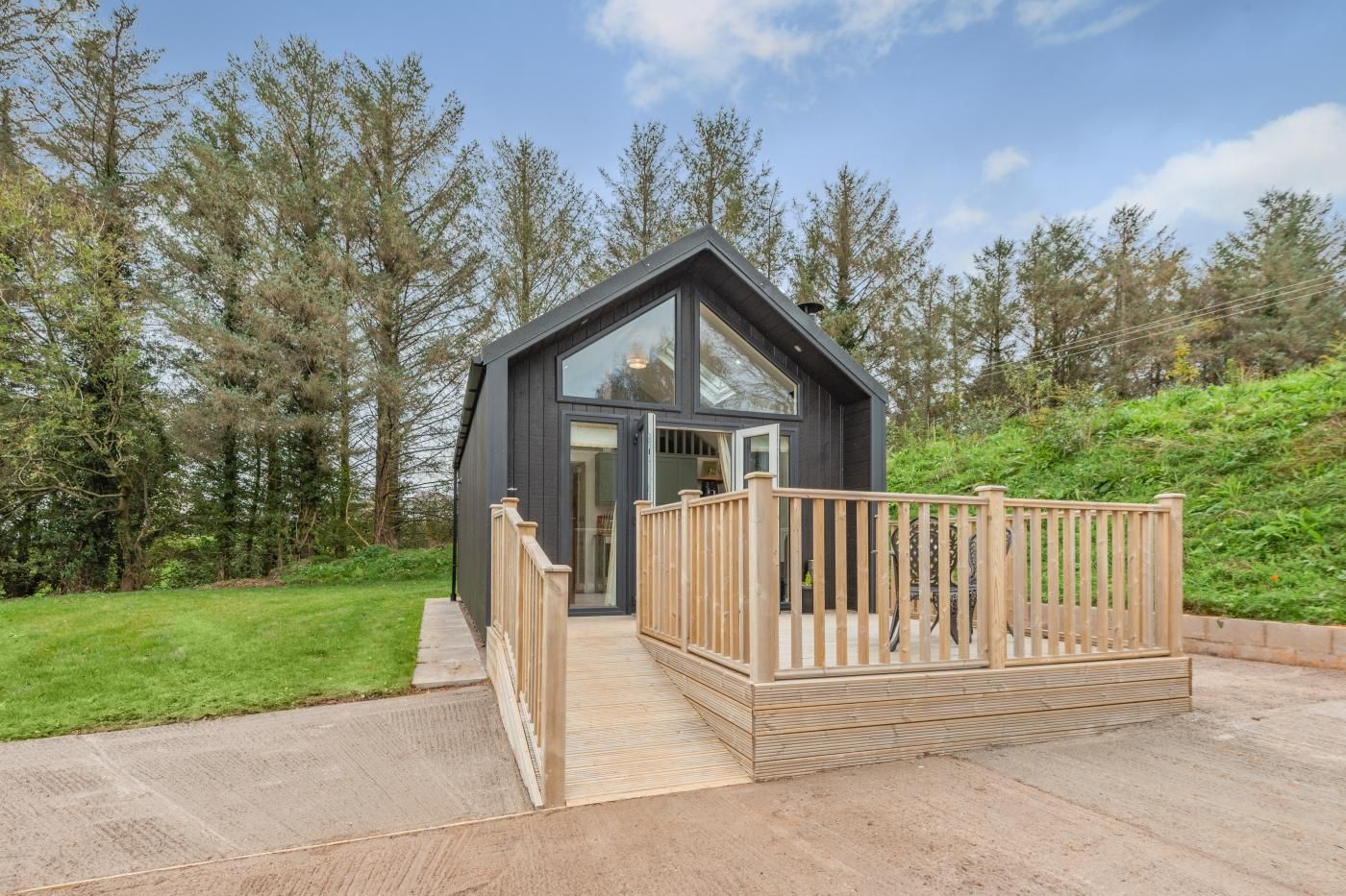 A modern cabin with a wooden deck, surrounded by trees.